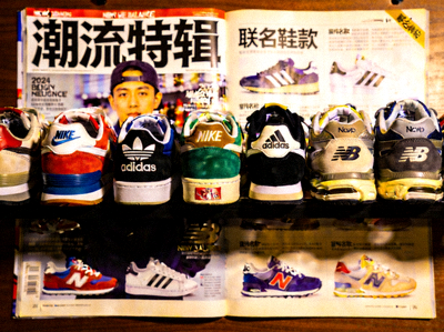 多双不同品牌的联名球鞋排列展示，包括Nike、Adidas和New Balance，背景是潮流杂志
