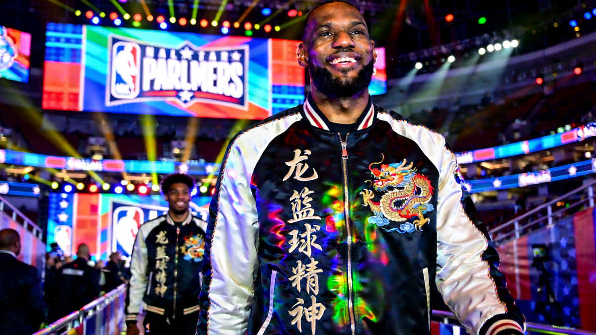 NBA全明星球员身着带有中国龙刺绣和汉字图案的潮流外套，在球员通道展示个性穿搭，背景是全明星赛场的灯光